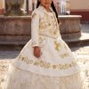 a girl wearing a traditional Mexican Charro dress , in Ivory color with gold embroidery in front of a fountain