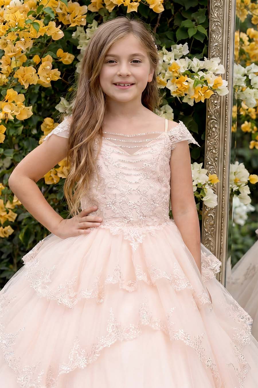 A girl wearing a pale blush multi layered dress with a white and yellow bugambilia background