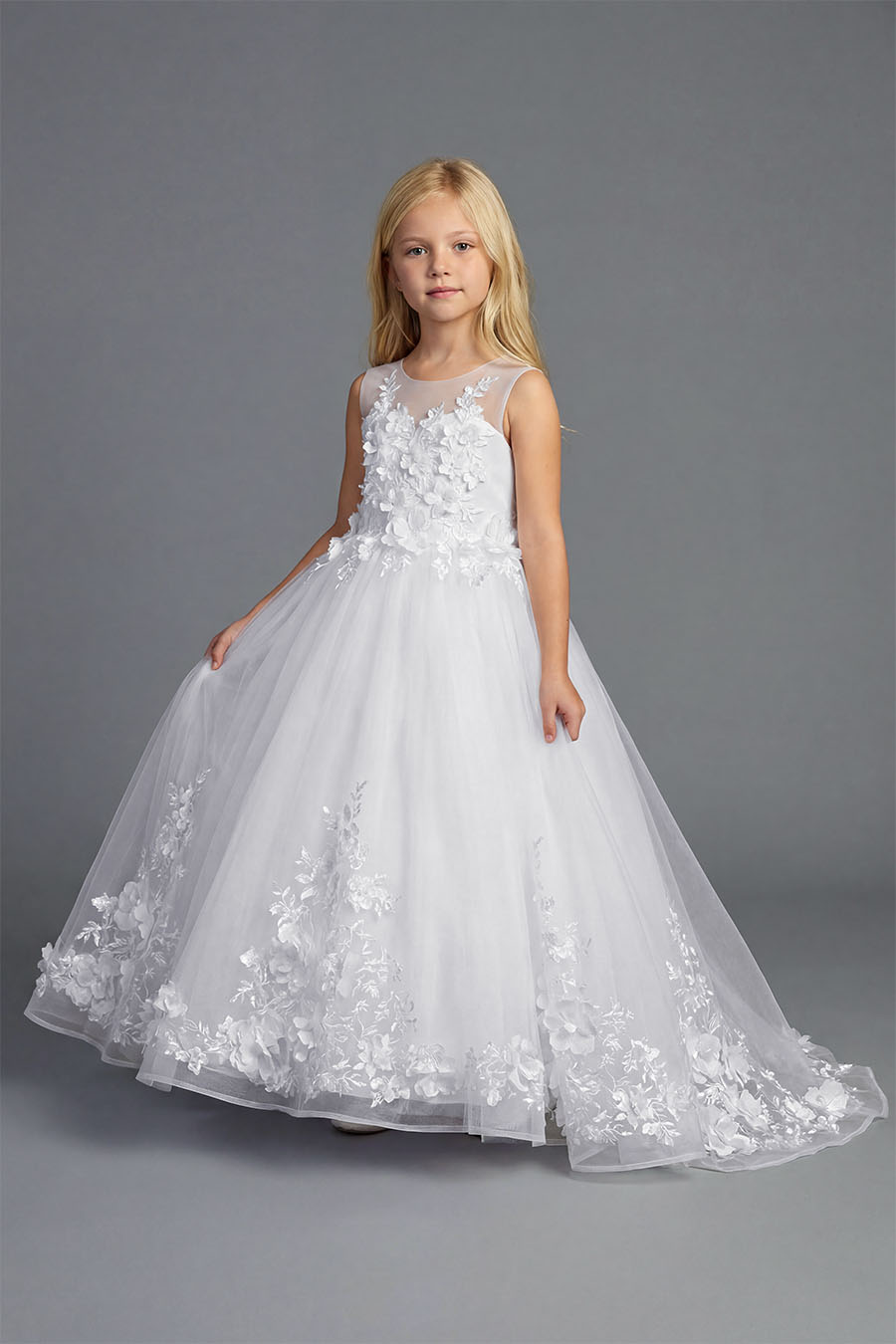 Young girl wearing a white sleeveless formal dress with floral appliqué bodice and full tulle skirt on a neutral background.